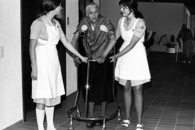 Historisches Bild aus dem Archiv: Zwei Pflegehelferinnen SRK stützen eine alte Frau beim Gehen.